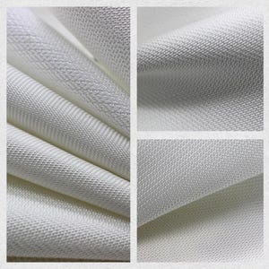 May include: Close-up of white fabric with a textured weave. The fabric is folded and layered, showcasing the detailed pattern and subtle variations in the material. The image highlights the texture and quality of the textile.