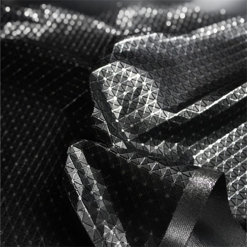 May include: A black fabric featuring a reflective, geometric grid pattern composed of small, raised triangular shapes. The material has a high-contrast, textured surface with bright white light points highlighting the edges of the grid structure.