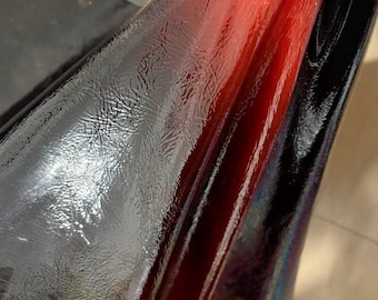 May include: Close-up of a glossy, textured material with a gradient of colors. The material transitions from black to a deep red, with highlights creating a reflective sheen. The surface appears to have a subtle, patterned texture.