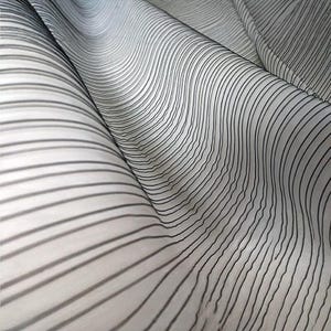 May include: Close-up of a flowing fabric with a white background and black, wavy, vertical stripes. The fabric is draped, creating soft curves and shadows. The stripes vary in thickness and spacing.
