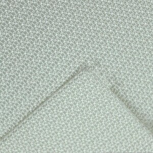 May include: Close-up of a light gray woven fabric with a textured, basketweave pattern. The fabric is folded over, revealing the underside. The weave is tight, creating a durable and visually interesting textile.