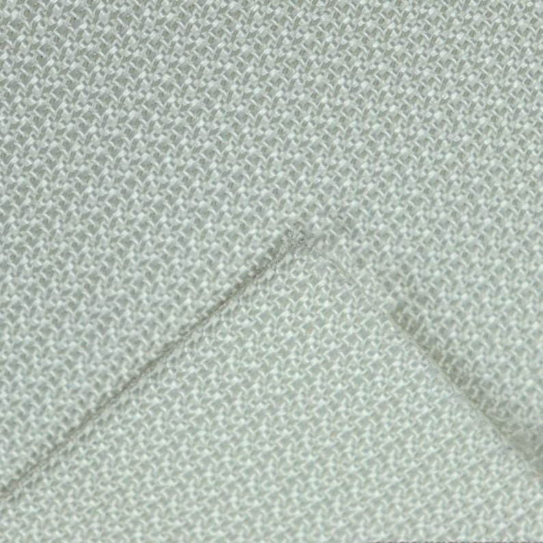 May include: Close-up of a light gray woven fabric with a textured, basketweave pattern. The fabric is folded over, revealing the underside. The weave is tight, creating a durable and visually interesting textile.