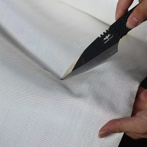 以下が含まれることがあります： 黒いナイフは、テクスチャ加工されたハンドルで、白い織物のロールをカットしています。生地はきつく織られており、耐久性があるようです。ナイフは銀色の刃とハンドルにロゴが付いています。