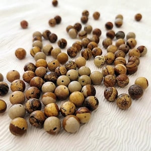 May include: A collection of round, natural stone beads in various shades of brown, tan, and cream. The beads have unique patterns and textures, with drilled holes for stringing. These beads are suitable for jewelry making and crafting.