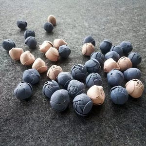 May include: A collection of small, fabric flower-shaped beads in shades of blue and tan. The beads are scattered on a gray surface, with some appearing to be in the process of being sewn.