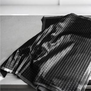 May include: A black fabric textile featuring a repeating geometric pattern of small white dots connected by thin white lines, creating a grid-like structure across the surface. The material is folded, showing depth and texture in the weave.