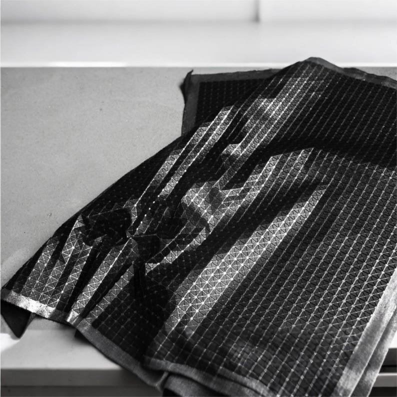 May include: A black fabric textile featuring a repeating geometric pattern of small white dots connected by thin white lines, creating a grid-like structure across the surface. The material is folded, showing depth and texture in the weave.