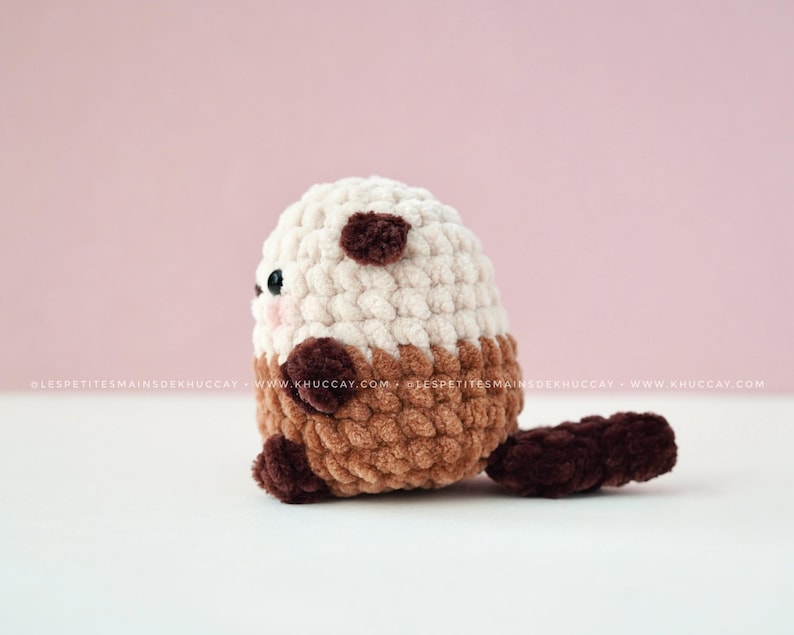 K&ouml;nnte beinhalten: Ein handgeh&auml;keltes Otter-Pl&uuml;schtier in Creme, Braun und Dunkelbraun. Das Stofftier hat einen abgerundeten K&ouml;rper, kleine Ohren und einen Schwanz. Das Gesicht des Otters hat kleine schwarze Augen und rosige Wangen.