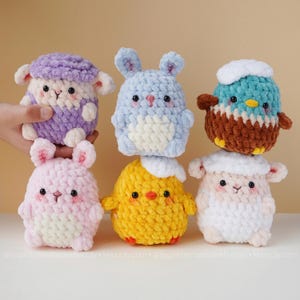 Puede incluir: Colección de seis animales de peluche de ganchillo hechos a mano en varios colores. Los juguetes incluyen una oveja morada, un conejo azul, un conejo rosa, un pollito amarillo, un pájaro turquesa y una oveja blanca. Cada juguete tiene ojos de seguridad negros y un diseño único.