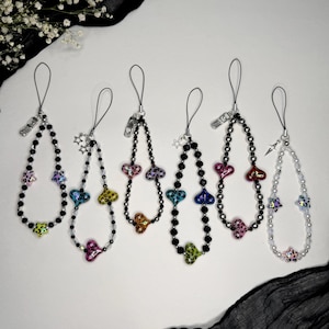 May include: Six phone charms featuring black or white beads, each accented with colorful heart or star-shaped charms with leopard print patterns. Each charm includes a thin black cord loop and a small silver-toned metal charm attachment.