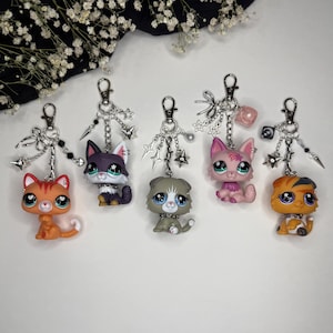 May include: Five keychains featuring stylized animal figures with large eyes, attached to silver-toned metal chains with lobster clasps. Each keychain includes decorative charms such as stars, spikes, bows, and beads in various colors and finishes.