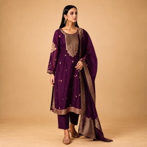 May include: A deep purple long-sleeved tunic with a round neckline, featuring a metallic gold embroidered panel on the chest, gold floral motifs across the fabric, a matching gold-bordered hem, straight-leg trousers, and a long matching shawl.