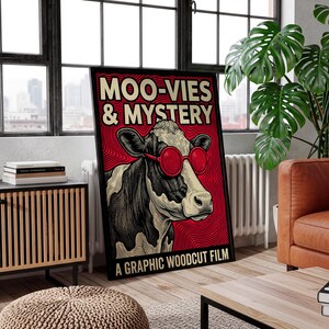May include: A framed graphic woodcut film poster with the text "MOO-VIES & MYSTERY." The poster features a black and white cow wearing red sunglasses against a red background. The poster is in a black frame.