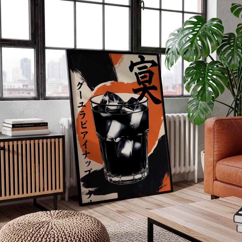 May include: A framed poster featuring a graphic illustration of a dark beverage with ice cubes in a glass. The poster has Japanese text and a background of orange and black brushstrokes. The poster is leaning against a window.