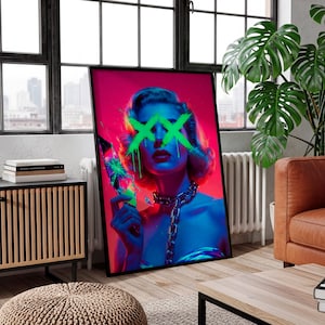 May include: A framed art print featuring a woman with green neon 'XX' marks over her eyes, holding a broken object. The artwork uses a vibrant color palette of pink, blue, and green, with a silver chain necklace. The print is displayed in a modern living room setting.