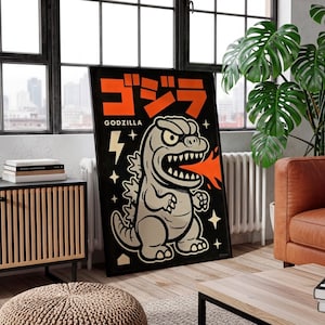 May include: A framed black poster featuring a cartoon Godzilla illustration. The poster has orange Japanese text and the English word "GODZILLA". The Godzilla character is gray with white teeth and is breathing orange fire. The background is black with white stars and a lightning bolt.