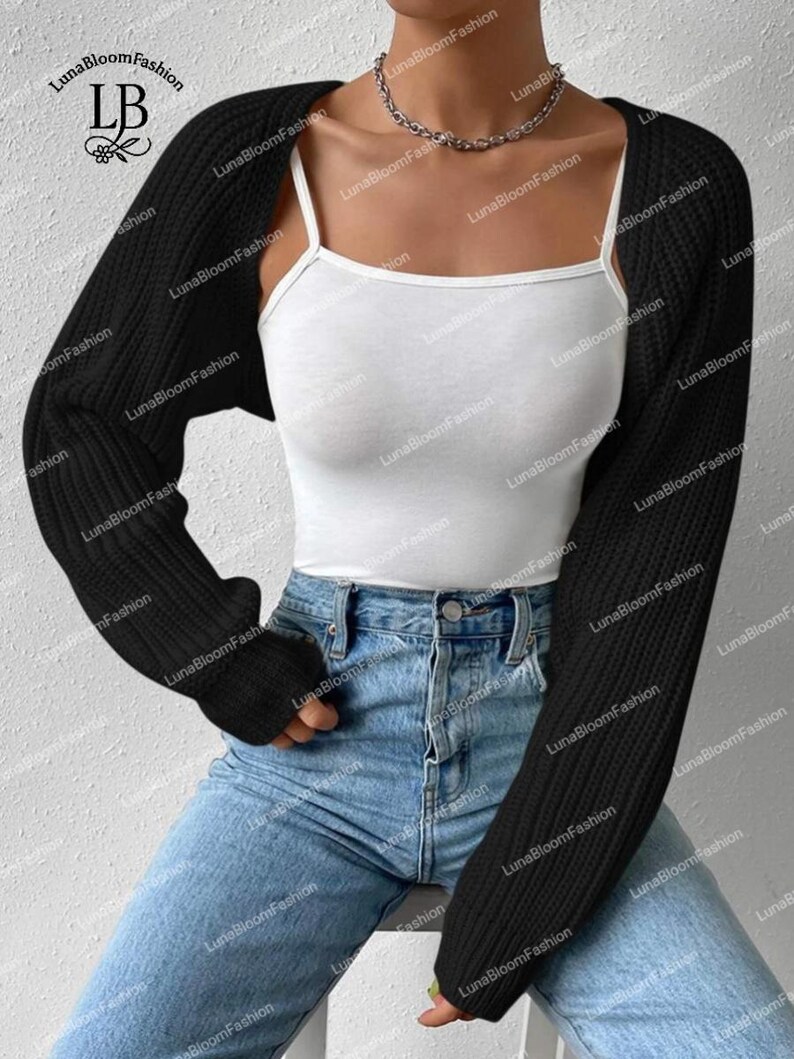 May include: A black, long-sleeved bolero cardigan. The cropped cardigan is worn over a white vest top and paired with blue jeans. A silver chain necklace is visible. The brand name "LunaBloomFashion" is printed on the image.