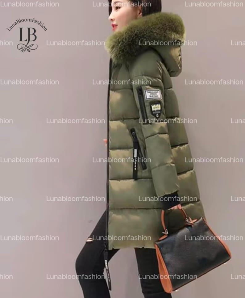 May include: Olive green puffer coat with a fur-trimmed hood. The long coat features a black zipper, a small patch on the sleeve, and a black handbag. The coat is designed for cold weather and is a stylish outerwear option.