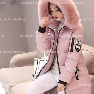 May include: A light pink puffer coat with a large, fluffy, light pink hood. The coat has a black zipper, black cuffs, and a small patch on the sleeve. The coat is knee-length and appears warm.