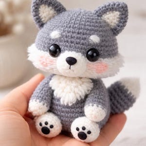 Peut inclure: Une peluche loup au crochet faite à la main, grise et blanche. L'animal en peluche a de grands yeux noirs, des joues roses et une poitrine et des pattes blanches. Le loup est assis et a une petite queue. Un jouet mignon et câlin.