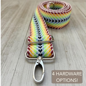 May include: A colorful woven strap with a rainbow chevron pattern, featuring a silver metal clasp and hardware. The strap is rolled up, with the text "4 HARDWARE OPTIONS!" in the bottom right corner.