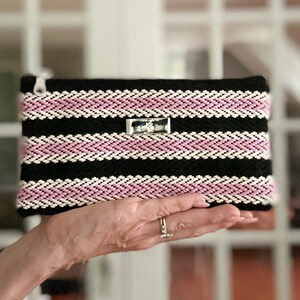 Cartera de cinta estampada en negro, rosa y blanco con ranuras para tarjetas integradas, bolsillo abierto y cierre de cremallera.