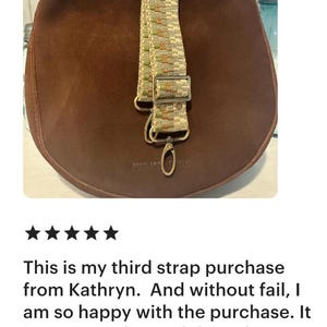 May include: A dark brown suede bag featuring a detachable woven shoulder strap. The strap displays a geometric pattern in beige, green, and orange tones, complemented by metallic hardware including a rectangular slider and a lobster clasp.