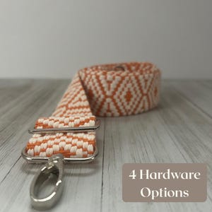 May include: An orange and white woven strap with silver-colored hardware. The strap is rolled up in the background. The text "4 Hardware Options" is in a brown rectangle in the bottom right corner.