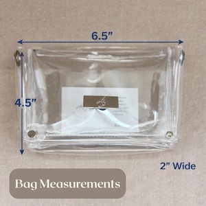 May include: A clear rectangular pouch with a silver-toned metal clasp featuring a logo. The bag measures 6.5 inches in length, 4.5 inches in height, and 2 inches in width. The design includes metal grommets on the sides and a zipper closure.