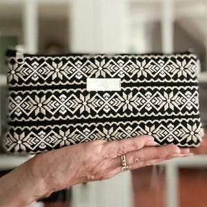 Cartera de cincha estampada en tonos tostados, negros y blancos con ranuras para tarjetas integradas, bolsillo abierto y cierre de cremallera.