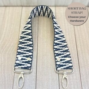 Könnte beinhalten: Ein kurzer Taschengurt mit einem schwarz-weißen Zickzackmuster. Der Gurt verfügt an beiden Enden über silberfarbene Metallkarabiner. Der Text auf dem Bild lautet: SHORT BAG STRAP! Choose your Hardware.