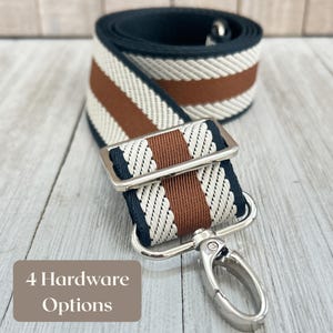 Puede incluir: Una correa de bolso a rayas azul marino, marrón y crema con herrajes plateados. La correa presenta un cierre y una hebilla de metal. El texto de la imagen dice "4 Hardware Options".