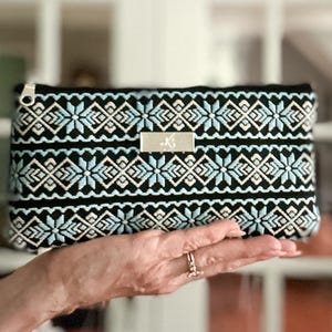 Cartera de cinta estampada en azul, negro y blanco con ranuras para tarjetas integradas, bolsillo abierto y cierre de cremallera.