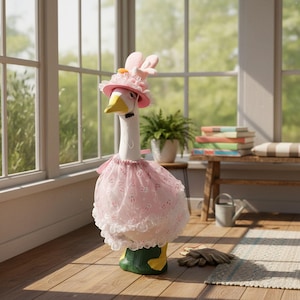 May include: A whimsical goose statue, adorned with a pink hat featuring bunny ears and a matching tutu. The goose has a yellow beak and green feet, creating a charming Easter or spring-themed decoration. The statue is set in a sunlit room.