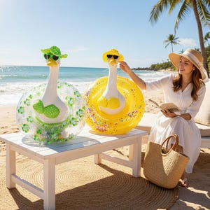 Puede incluir: Dos flotadores inflables de ganso con gafas de sol y sombreros. Uno es transparente con detalles verdes, el otro es amarillo. Están sobre una mesa blanca en una playa de arena.