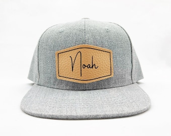 May include: Grey baseball cap with a brown leather patch that says "Noah" in a cursive font.
