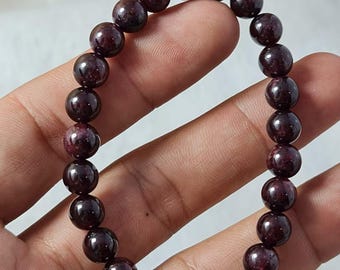May include: A dark red beaded bracelet. The bracelet is made of round, polished beads with a deep burgundy color. The beads are strung together on an elastic band, creating a flexible and comfortable fit. The bracelet is shown on a hand.