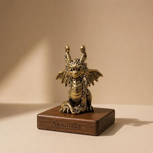 May include: A brass dragon ornament with detailed wings and horns, sitting on a dark wooden base. The base is engraved with the name "Alexander". The dragon has intricate scales and a smiling face. The overall theme is fantasy.