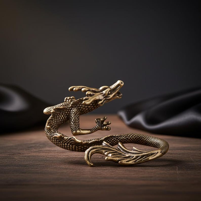 Op de afbeelding: Een messingkleurig metalen drakenbeeldje met ingewikkelde schubstructuren, een gebogen lichaam, een opgeheven kop met open mond en een lange, vloeiende staart. Het beeldhouwwerk heeft een metallic afwerking met donkere accenten in de diepere delen.