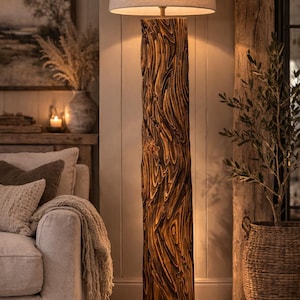 May include: A tall, wooden floor lamp with a textured, carved design. The lamp has a beige fabric shade and stands on a black base. The wood has a warm, brown tone, and the lamp is placed in a cozy living room setting.