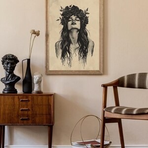 May include: A framed wall art print featuring a black ink illustration of a person with long hair and a crown of roses. The person has their head tilted back with eyes closed. The artwork is set against a light beige, textured background.
