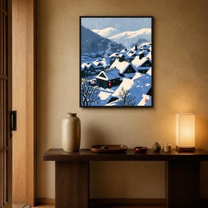 May include: A framed wall art print depicting a snowy village scene with dark-roofed houses covered in thick white snow, bare trees, and distant blue mountains under a clear sky. A single red lantern glows near a house with rising chimney smoke.