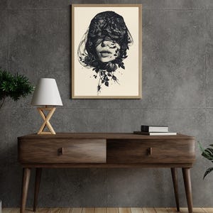 Op de afbeelding: Een ingelijste muurkunstprint met een zwart-witillustratie van een gezicht dat gedeeltelijk wordt bedekt door donkere rozen en vloeiende stof. Het kunstwerk staat op een lichte cr&egrave;mekleurige achtergrond in een eenvoudige houten lijst.