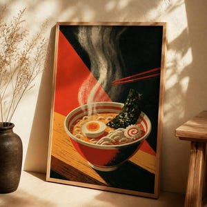 May include: A framed art print featuring a bowl of ramen with noodles, a soft-boiled egg, a slice of narutomaki, and a sheet of nori. The illustration uses a bold color palette of red, black, and yellow with steam rising from the bowl.