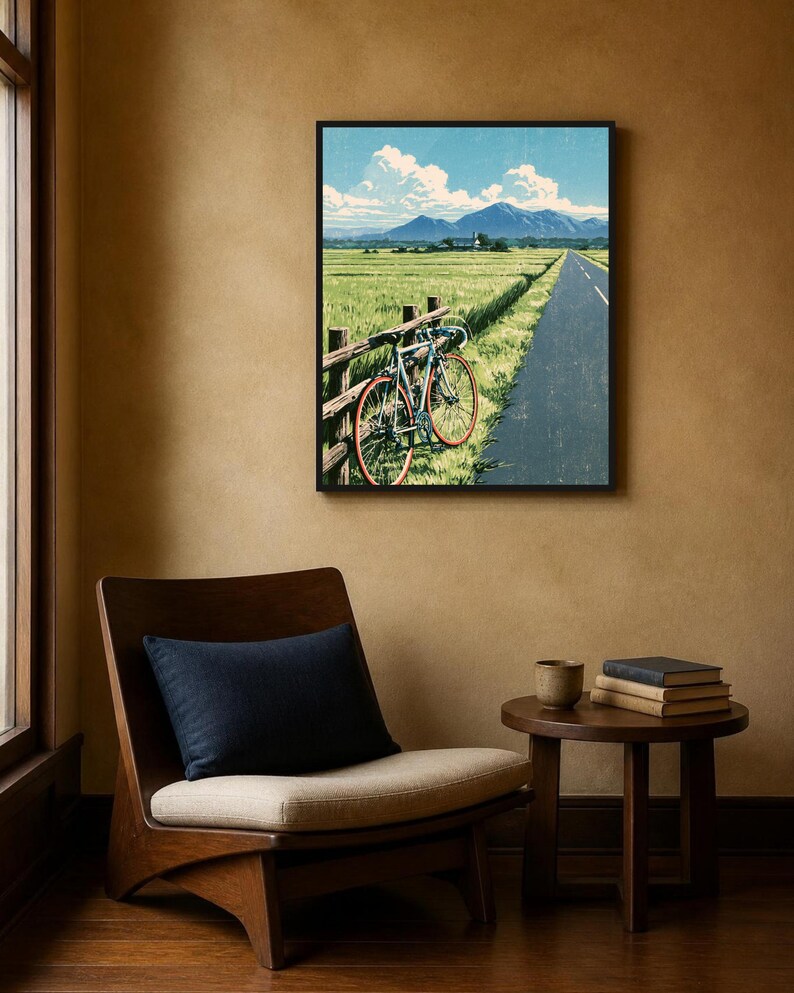 May include: A framed wall art print depicting a landscape scene with a bicycle leaning against a wooden fence beside a paved road, overlooking a green field with distant mountains under a blue sky with white clouds.