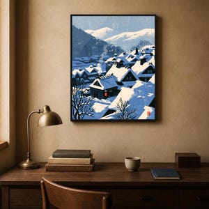 May include: A framed art print depicting a snowy village scene with dark houses featuring steep roofs covered in thick white snow. The landscape includes distant blue mountains, bare trees, and a single bright red circular lantern accent.