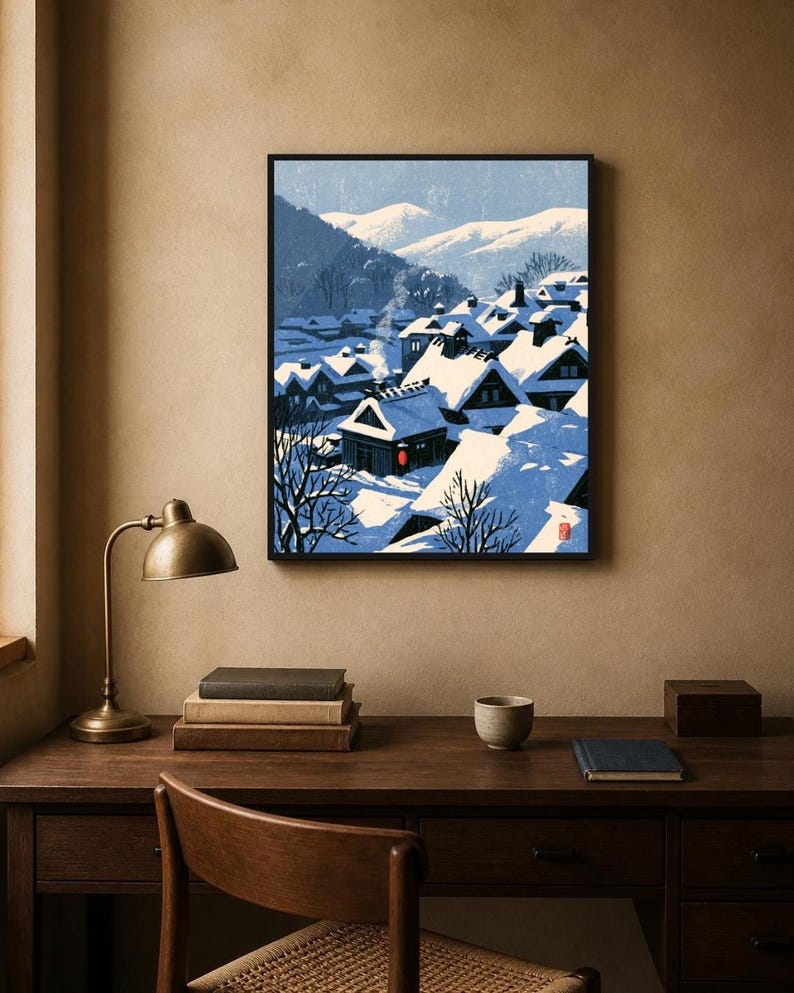 May include: A framed art print depicting a snowy village scene with dark houses featuring steep roofs covered in thick white snow. The landscape includes distant blue mountains, bare trees, and a single bright red circular lantern accent.