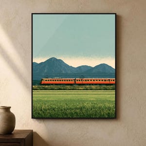 May include: A framed wall art print featuring a landscape illustration of an orange and red train travelling horizontally across a green field. In the background, dark blue mountains are visible under a pale blue sky with a soft horizon line.