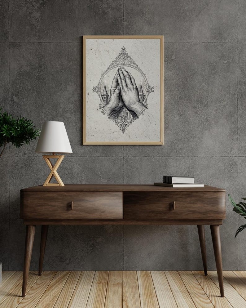 Op de afbeelding: Een ingelijste wandkunstprint met een gedetailleerde zwart-witillustratie van twee handen die in gebed zijn samengevouwen, omsloten door een sierlijk decoratief frame met kleine kerktorens aan weerszijden, tegen een lichte, getextureerde achtergrond.
