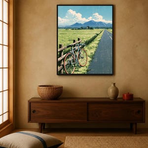 May include: A framed wall art print depicting a landscape scene with a bicycle leaning against a wooden fence beside a paved road. The image features a green field, distant blue mountains, and a bright blue sky with white clouds.